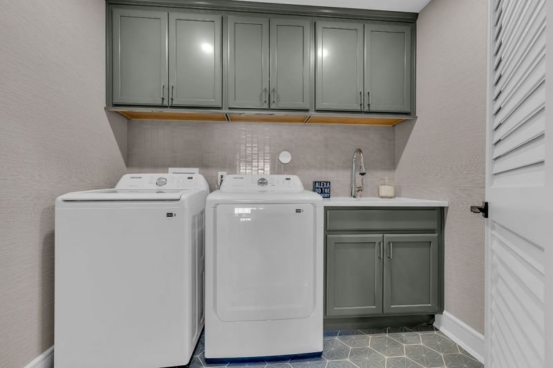 Interior photo of the Lockwood model at the Grove at Woodhaven showing the laundry room with porcelain tiles, a full-size washer and dryer, and a sink with newly installed cabinetry for added storage.