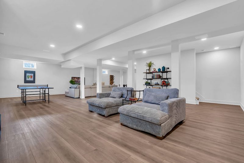 Interior photo of the Lockwood model at the Grove at Woodhaven showing the finished basement. The space features luxurious oak flooring, several seating areas with couches, tables, and chairs, as well as a table tennis setup. The space features elegant decor and artwork.