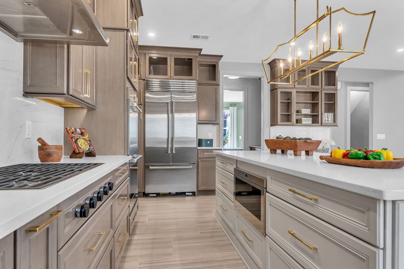 Interior photo of the Sequoia model at the Grove at Woodhaven showing another angle of the modern eat-in kitchen with luxurious oak flooring, stainless steel appliances, new cabinetry, and white quartz countertop with a white marble backsplash. An elegant chandelier hangs above the kitchen island.
