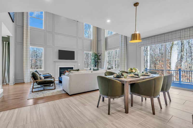 Interior photo of the Sequoia model at the Grove at Woodhaven showing another angle of the open-floor concept of the eat-in-kitchen and family room together. The layout features a six-person seating area including a table and chairs, along with a large couch in the family room. High vaulted ceilings with large windows are included.