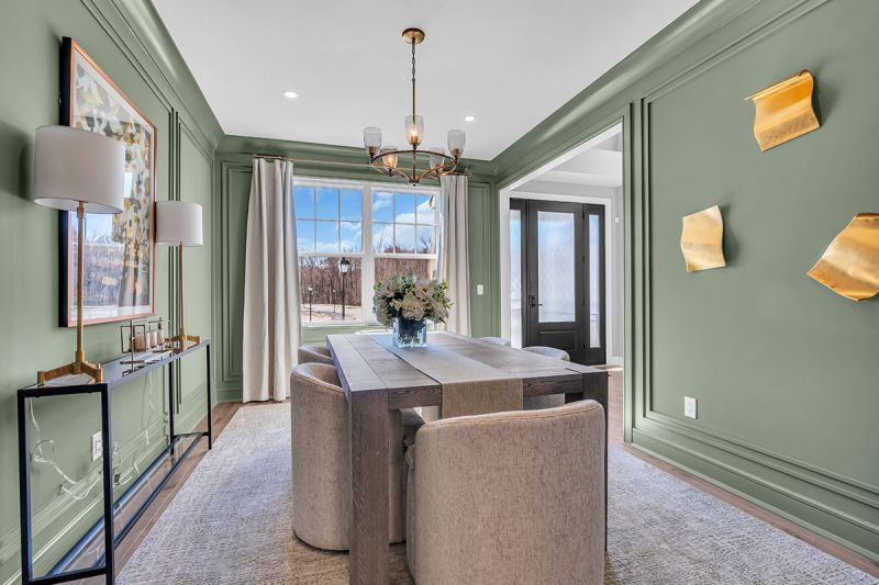 Interior photo of the Sequoia model at the Grove at Woodhaven showcasing the dining room with luxurious wood flooring. An elegant chandelier hangs above a six-person table surrounded by chairs. The space features elegant decor and artwork. There is a large window to allow in natural light.
