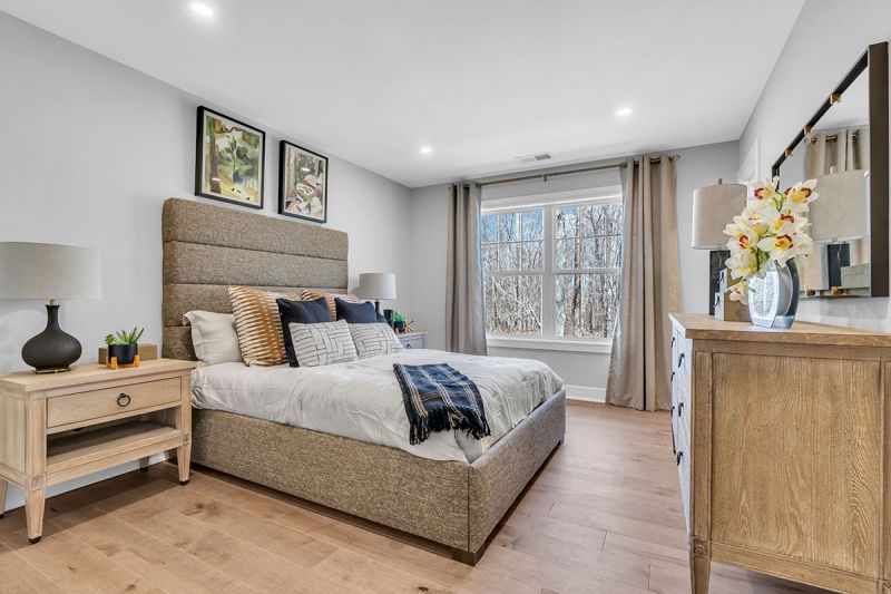 Interior photo of the Sequoia model at the Grove at Woodhaven showing the fourth bedroom featuring luxury wood flooring, a bed with two nightstands on each side and a dresser. A large window can be seen to allow in natural light.